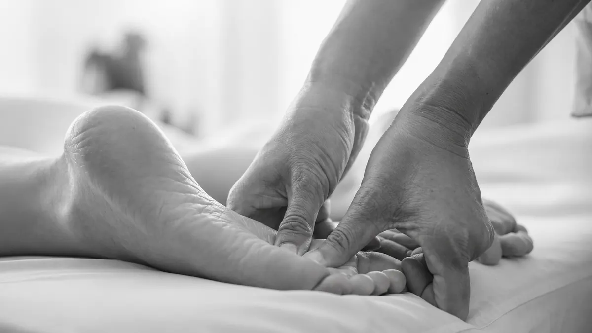 A remedial therapist providing hands-on foot treatment for an older adult.